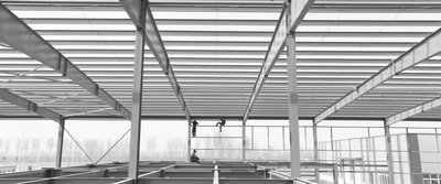 Metallträgerstruktur, an deren Ende drei Arbeiter handwerklich tätig sind.