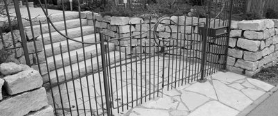 Geschwungener Zaun vor einem Garteneingang mit steinerner Treppe und Boden
