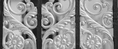 Verzierte, metallische Gitterstruktur mit kunstvoll geschwungenen Ornamenten, typisch für dekorative Metalllackierungen.