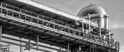 industrielle Rohre und Konstruktionen, mit großen Metallkanälen und einem Gitterwerk vor einem klaren Himmel.